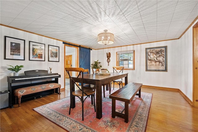 dining space with crown molding, a barn door, wood-type flooring, and an inviting chandelier