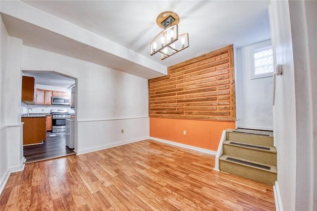 unfurnished dining area with a notable chandelier, baseboards, and light wood-type flooring
