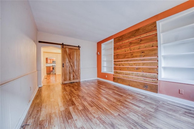 spare room with arched walkways, a barn door, built in features, light wood finished floors, and baseboards