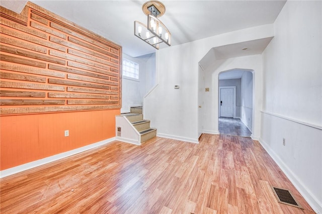 empty room with visible vents, light wood-style floors, baseboards, arched walkways, and stairs