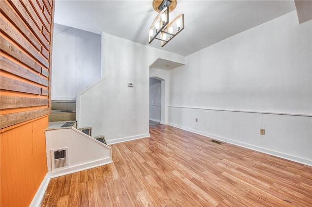 unfurnished dining area with light wood-style flooring, visible vents, baseboards, arched walkways, and stairs