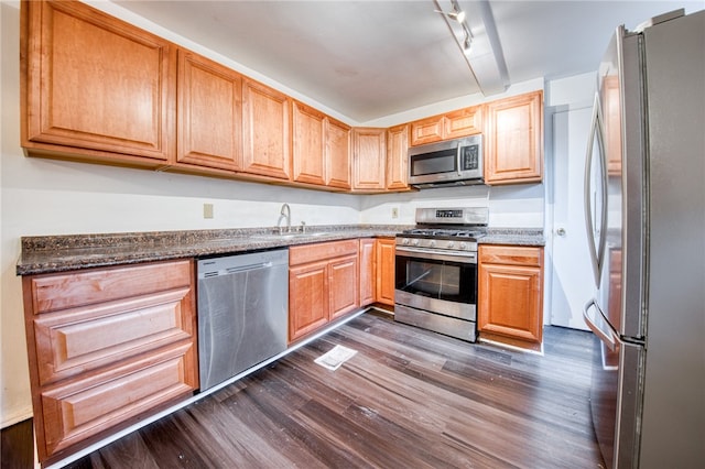 kitchen with dark hardwood / wood-style floors, stainless steel appliances, dark stone counters, sink, and rail lighting