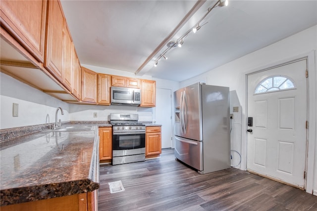 kitchen featuring dark hardwood / wood-style floors, dark stone counters, sink, rail lighting, and appliances with stainless steel finishes