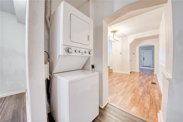 clothes washing area featuring light wood finished floors, stacked washing maching and dryer, a notable chandelier, laundry area, and arched walkways