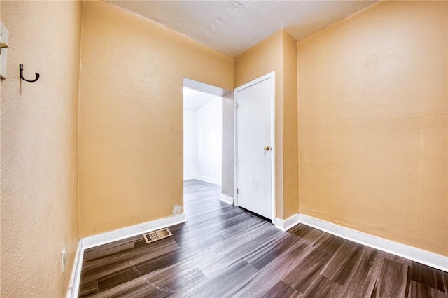 spare room featuring visible vents, baseboards, and dark wood-type flooring