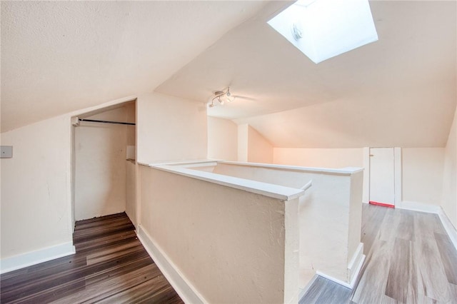 additional living space featuring vaulted ceiling with skylight, wood finished floors, and baseboards