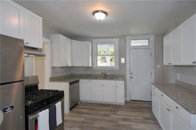 kitchen featuring appliances with stainless steel finishes, light stone counters, wood-type flooring, and white cabinetry