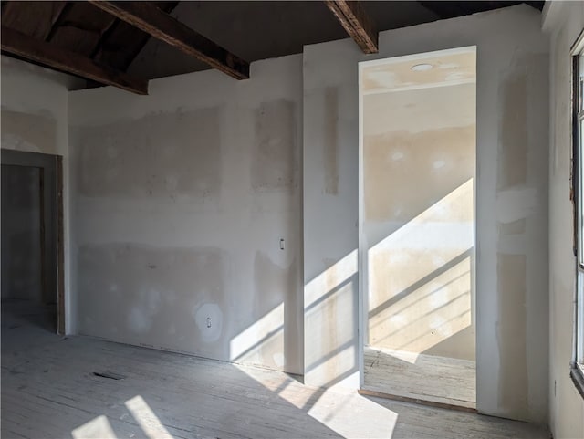 unfurnished room with beam ceiling and light wood-type flooring