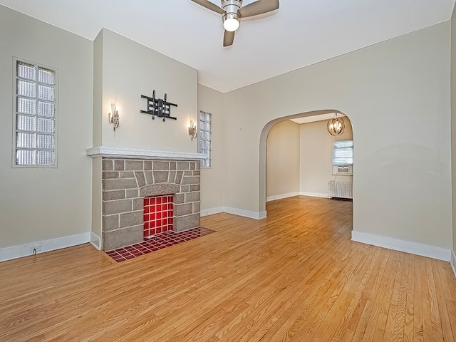 unfurnished living room with ceiling fan, a stone fireplace, and hardwood / wood-style floors