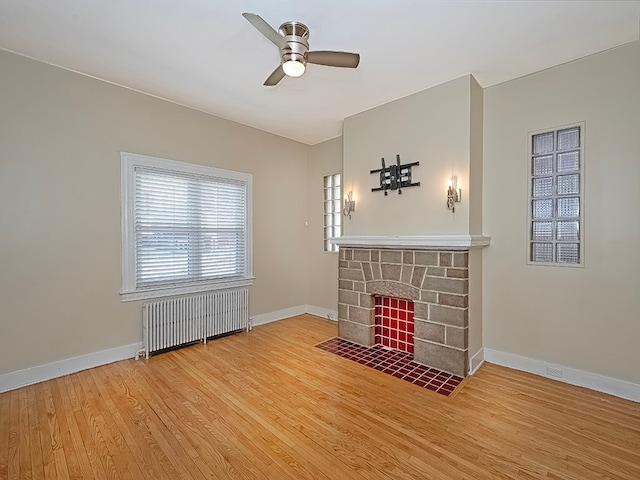 unfurnished living room with a stone fireplace, radiator heating unit, hardwood / wood-style floors, and ceiling fan