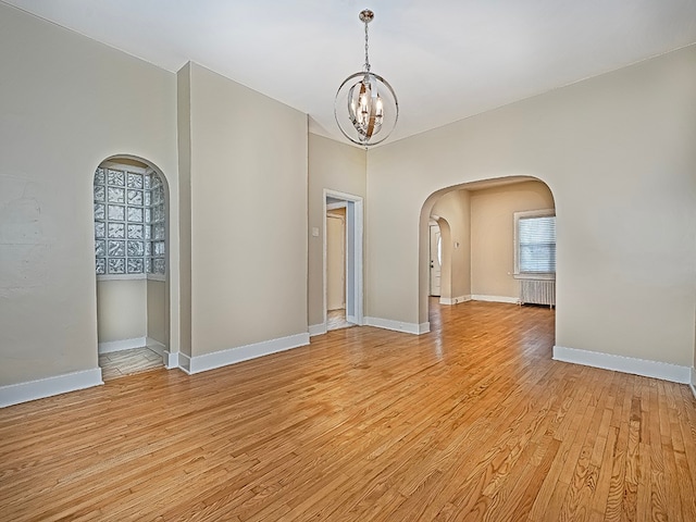 spare room featuring a notable chandelier and light wood-type flooring