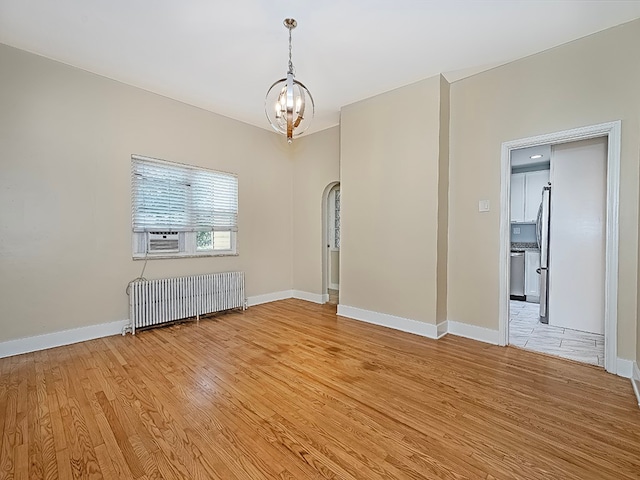 unfurnished room with light hardwood / wood-style flooring, a notable chandelier, and radiator