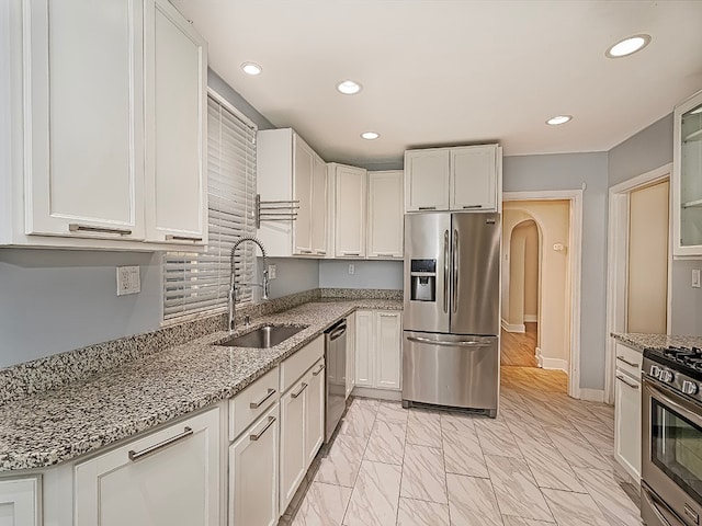 kitchen featuring white cabinetry, light stone counters, stainless steel appliances, and sink