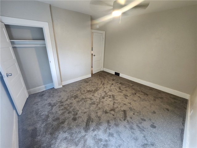 unfurnished bedroom with dark colored carpet, a closet, and ceiling fan