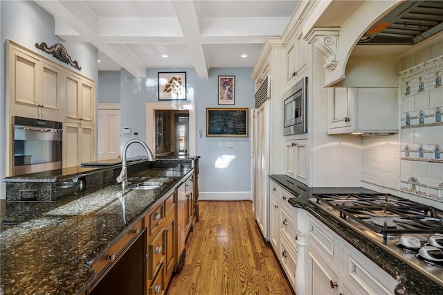 kitchen featuring stainless steel appliances, tasteful backsplash, light hardwood / wood-style flooring, beamed ceiling, and dark stone counters