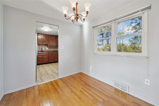 unfurnished dining area featuring an inviting chandelier, light hardwood / wood-style flooring, and sink