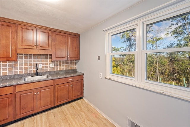 kitchen featuring light hardwood / wood-style floors, decorative backsplash, sink, and dark stone counters