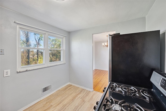 kitchen with light hardwood / wood-style floors, a notable chandelier, and black gas range oven