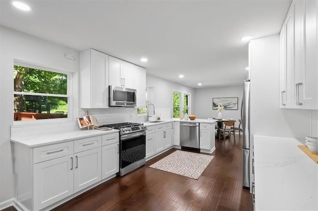 kitchen featuring dark hardwood / wood-style floors, kitchen peninsula, sink, white cabinets, and appliances with stainless steel finishes