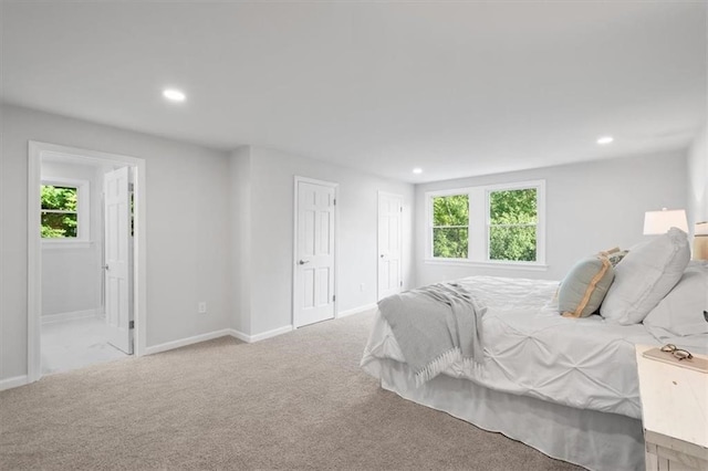 bedroom with light carpet, multiple windows, and ensuite bath