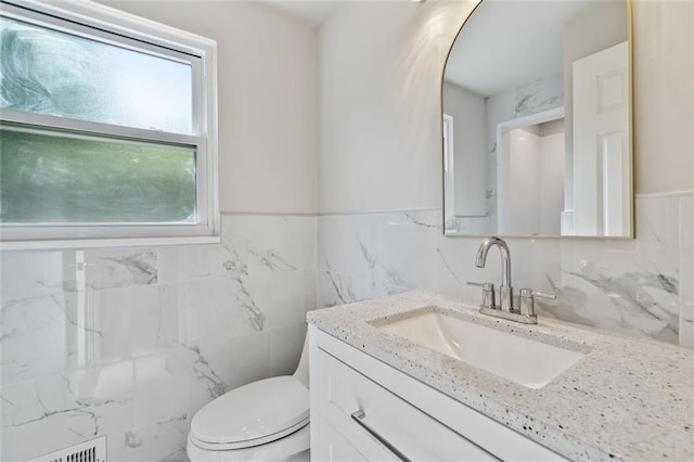 bathroom with tile walls, vanity, toilet, and plenty of natural light