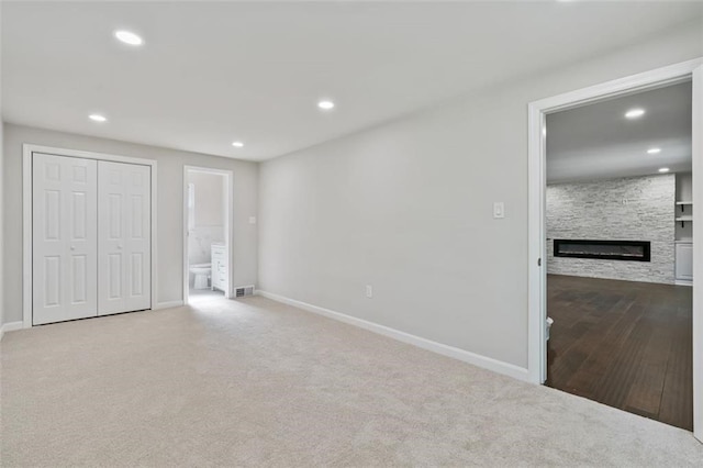 unfurnished bedroom with light carpet, a fireplace, ensuite bathroom, and a closet