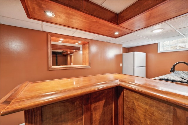 bar with a drop ceiling, wood counters, white fridge, and sink