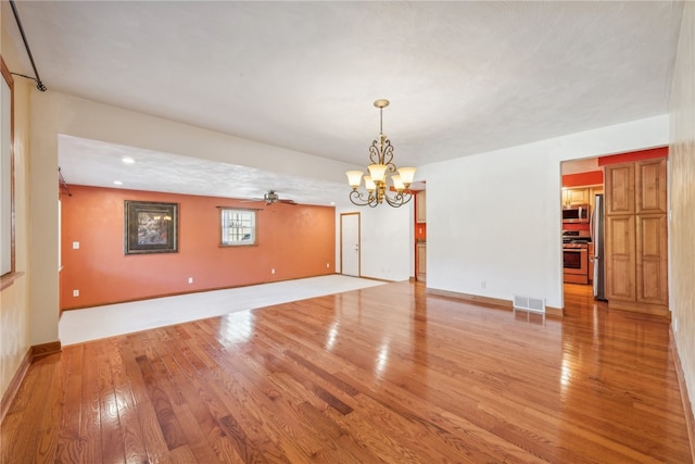 empty room featuring ceiling fan with notable chandelier and light wood-type flooring