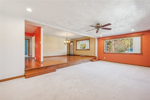 unfurnished living room with ceiling fan with notable chandelier, carpet flooring, and a healthy amount of sunlight