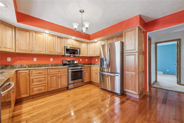 kitchen with light stone countertops, pendant lighting, an inviting chandelier, appliances with stainless steel finishes, and light hardwood / wood-style floors