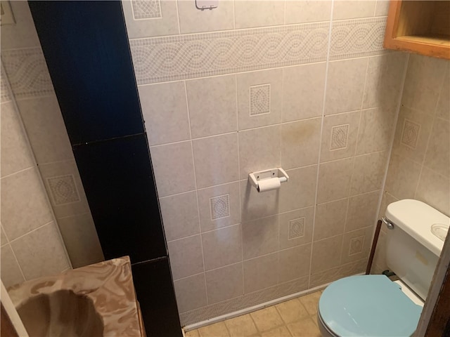 bathroom featuring toilet, tile patterned floors, and tile walls