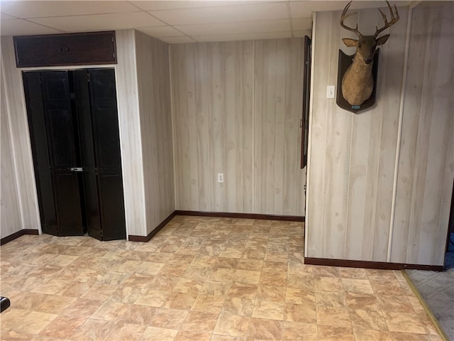 unfurnished room featuring a drop ceiling and wood walls