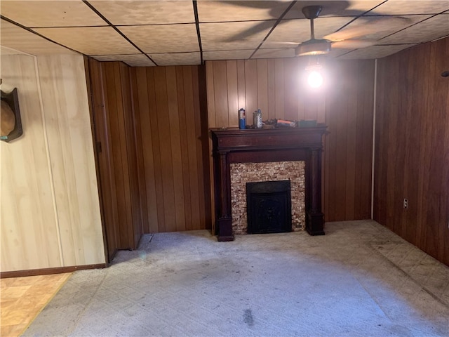 unfurnished living room featuring a stone fireplace, a drop ceiling, light colored carpet, and wooden walls