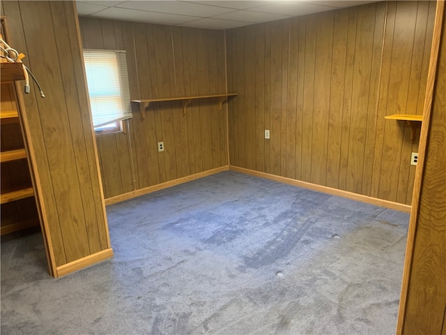 carpeted empty room with a paneled ceiling and wood walls