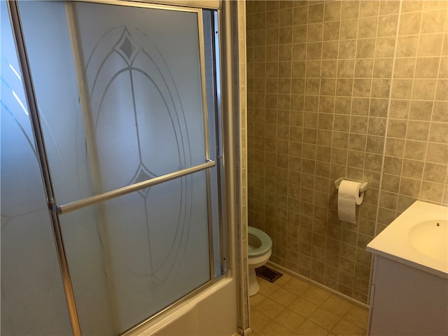 full bathroom with tile walls, shower / bath combination with glass door, toilet, vanity, and tile patterned floors