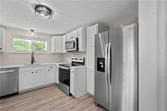 kitchen with sink, a textured ceiling, stainless steel appliances, white cabinets, and light hardwood / wood-style flooring