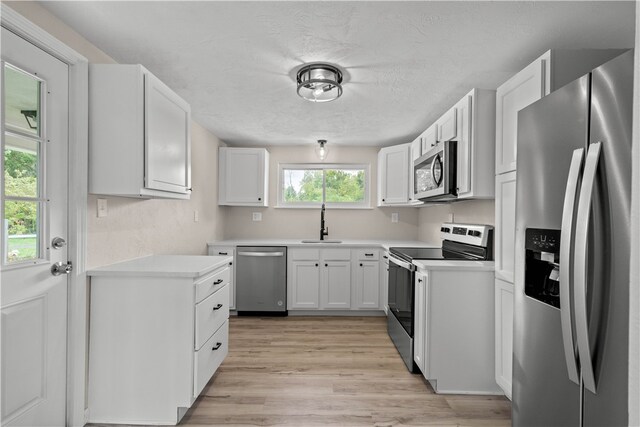 kitchen with appliances with stainless steel finishes, white cabinetry, a textured ceiling, light hardwood / wood-style flooring, and sink