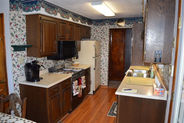 kitchen featuring a textured ceiling, black appliances, sink, and light wood-type flooring