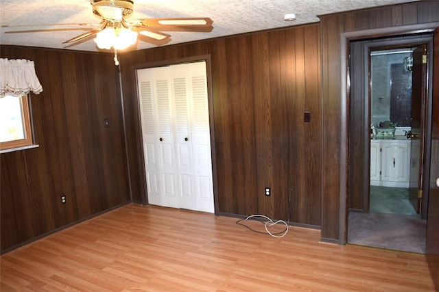 unfurnished bedroom featuring a closet, wooden walls, light hardwood / wood-style flooring, a textured ceiling, and ceiling fan