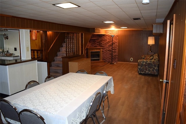 dining space featuring hardwood / wood-style floors, wooden walls, and a brick fireplace