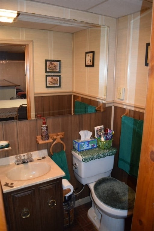 bathroom featuring vanity, toilet, tile patterned floors, and wooden walls