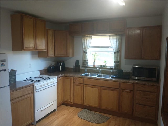kitchen featuring white appliances, a sink, light wood finished floors, brown cabinets, and dark countertops