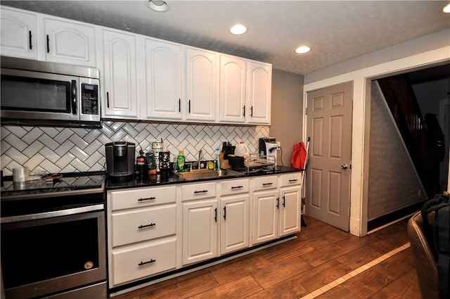 kitchen featuring white cabinetry, appliances with stainless steel finishes, dark hardwood / wood-style flooring, decorative backsplash, and sink