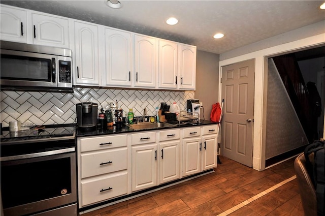 kitchen featuring stainless steel appliances, a sink, white cabinetry, dark countertops, and backsplash