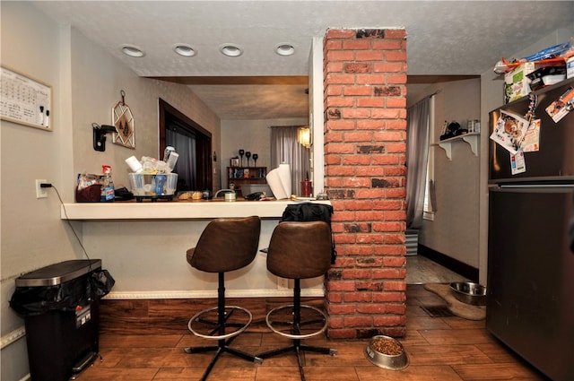 kitchen with black fridge, dark hardwood / wood-style floors, and a kitchen breakfast bar