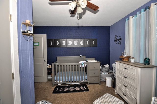 carpeted bedroom with a crib and ceiling fan