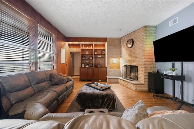 living room with light hardwood / wood-style floors, wood walls, a textured ceiling, and a brick fireplace