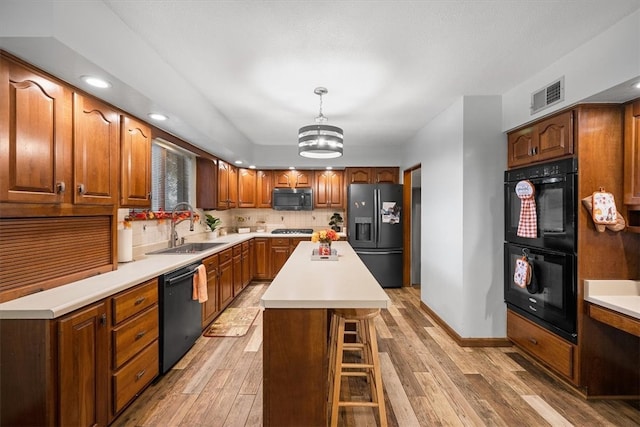 kitchen featuring a kitchen island, hanging light fixtures, sink, black appliances, and light wood-type flooring