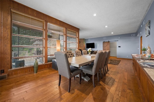 dining room with a healthy amount of sunlight, a barn door, a textured ceiling, and light hardwood / wood-style floors