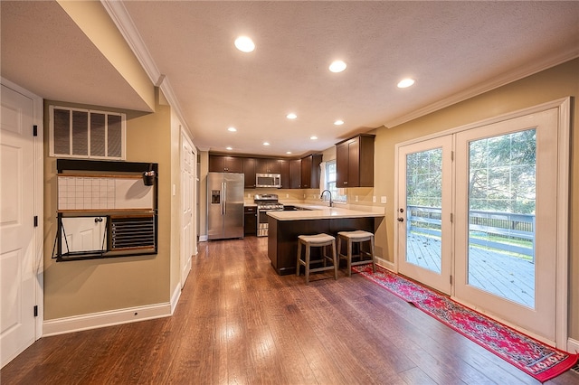 kitchen featuring a kitchen bar, kitchen peninsula, stainless steel appliances, crown molding, and dark hardwood / wood-style floors